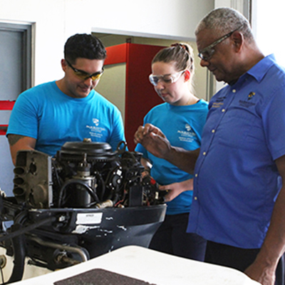 Two students and a teacher looking at a boat motor